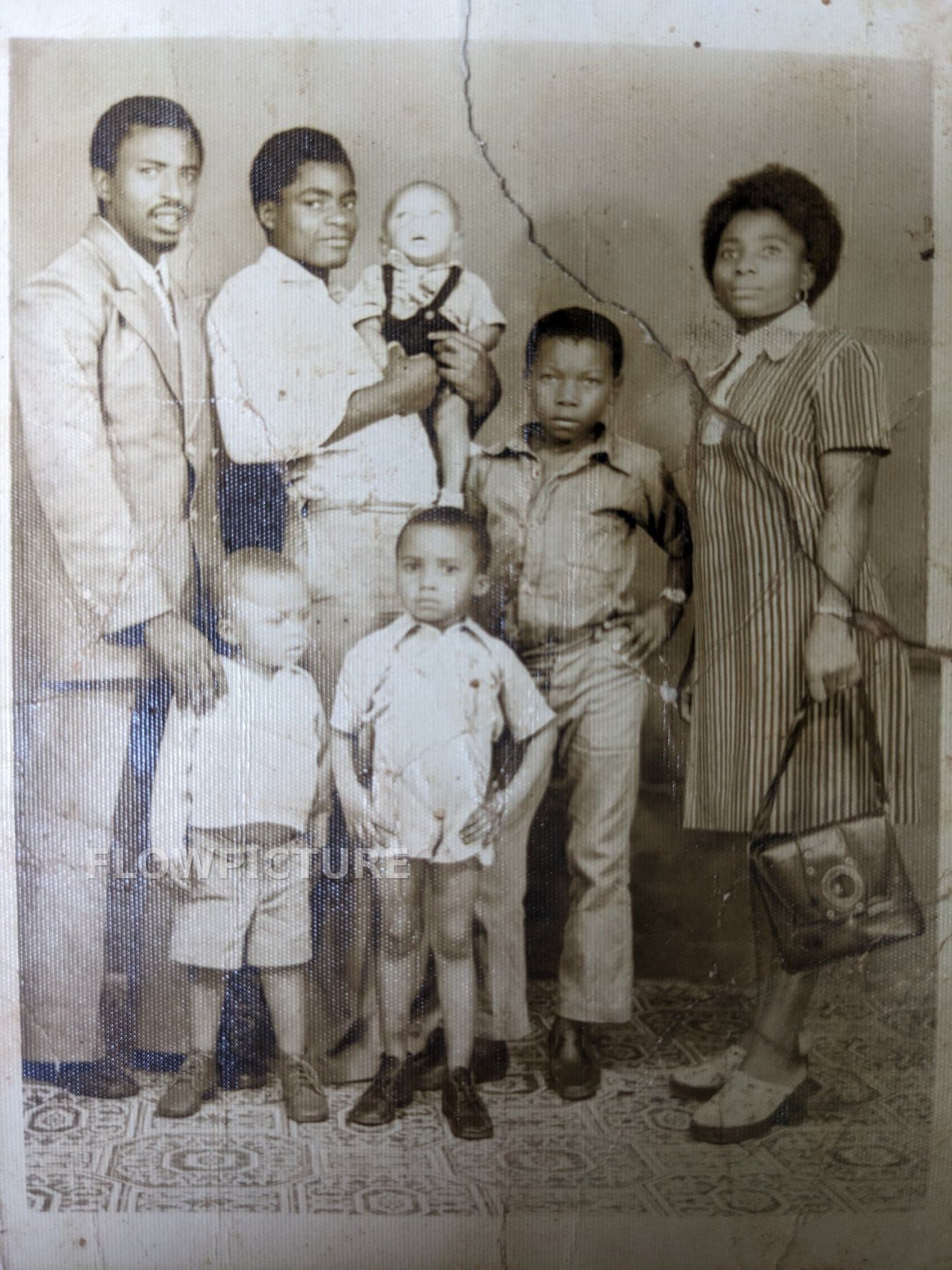 Family portrait of eight people: the original print is cracked in two and faded, the restored version is sharp and colourised