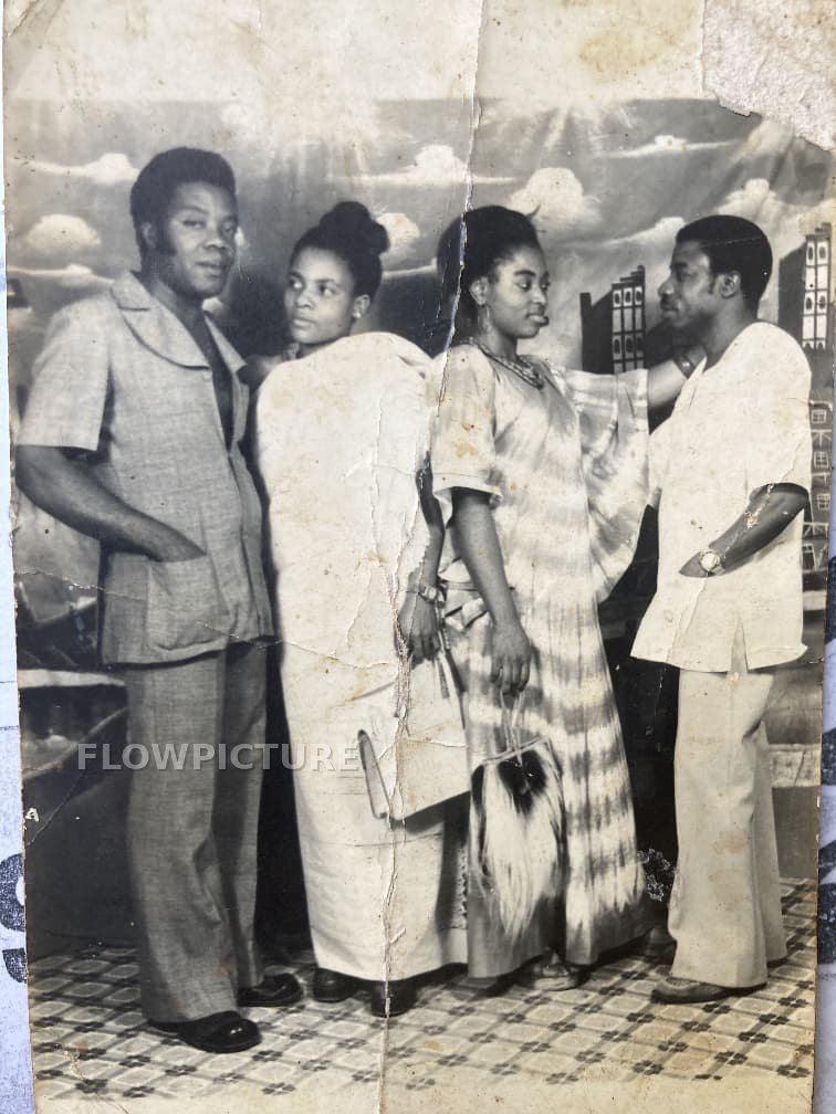 Group of four people in front of a painted backdrop, from black and white to colour