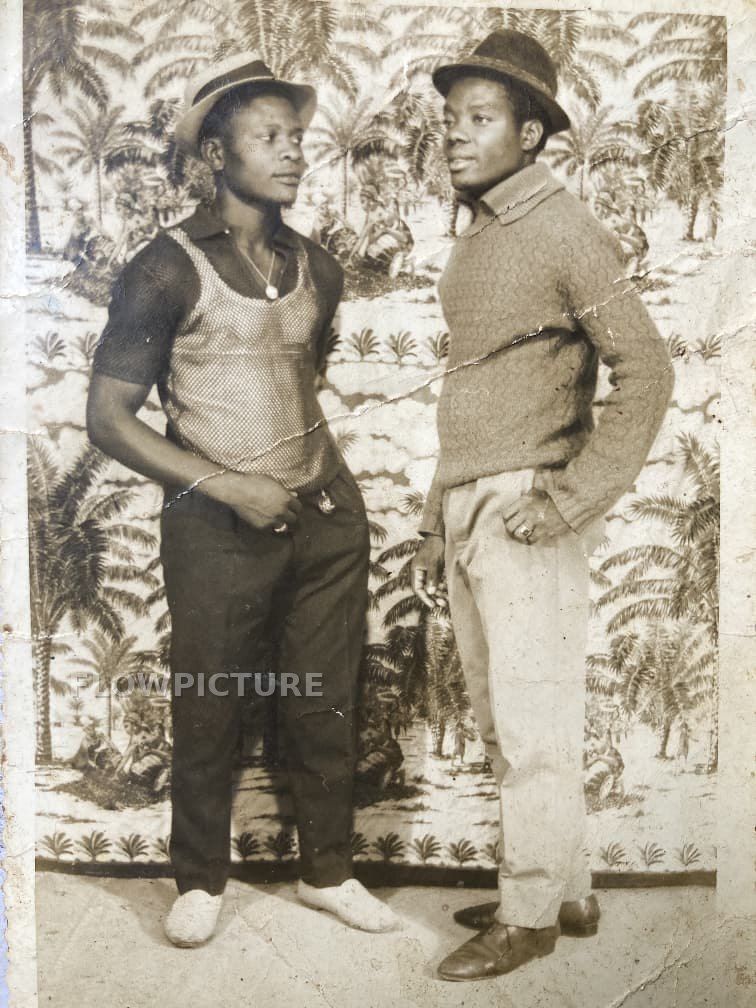 Two men posing in front of a patterned drape, from black and white to colour